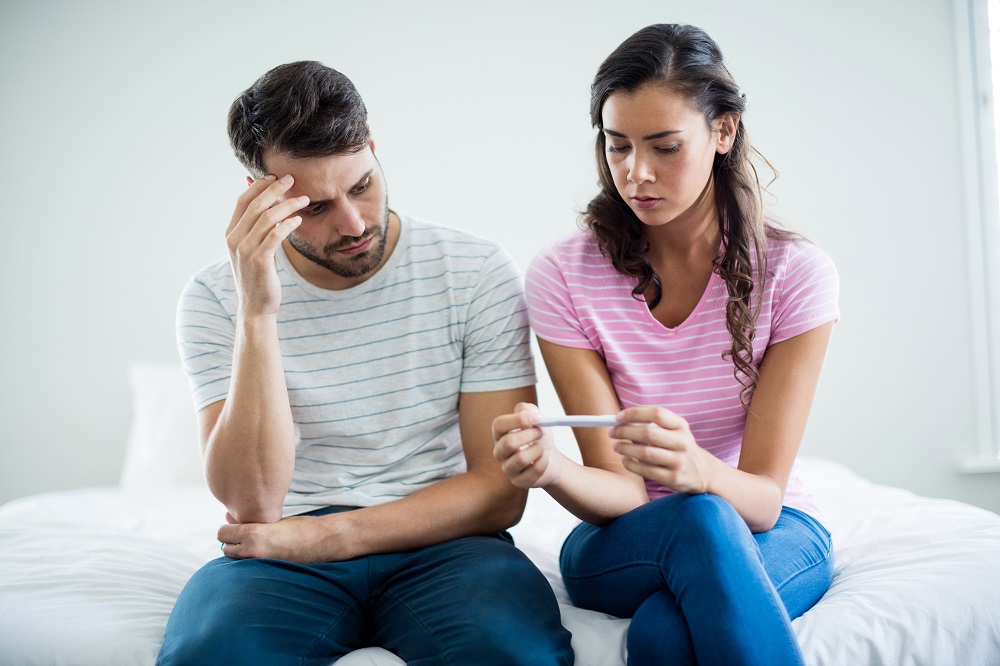 Worried couple finding out results of a pregnancy test in bedroom at home